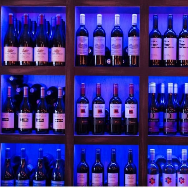 A wine display at Vino Cappuccino with multiple bottles of red wine illuminated by blue lights.