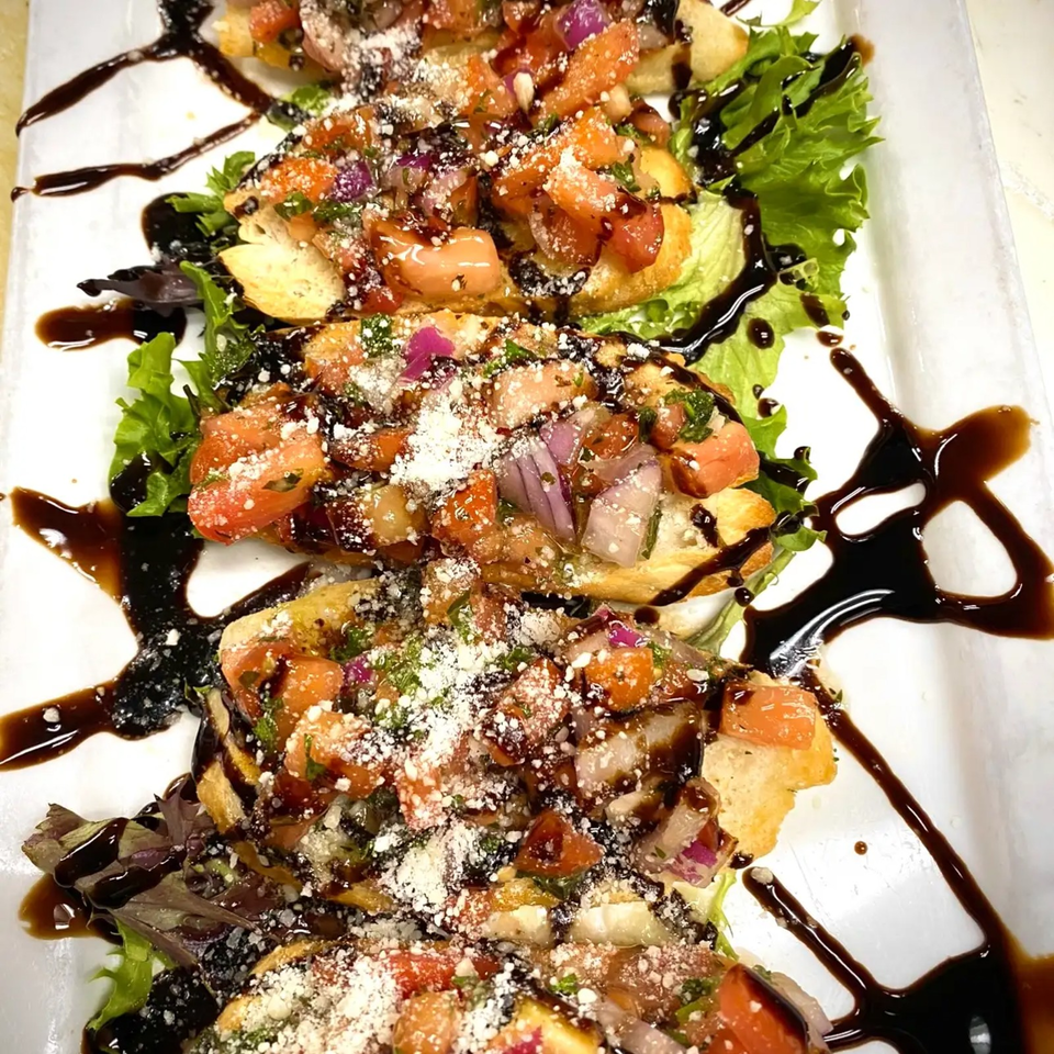 Bruschetta slices topped with diced tomatoes, red onion, herbs, and cheese, arranged over lettuce with balsamic drizzle.