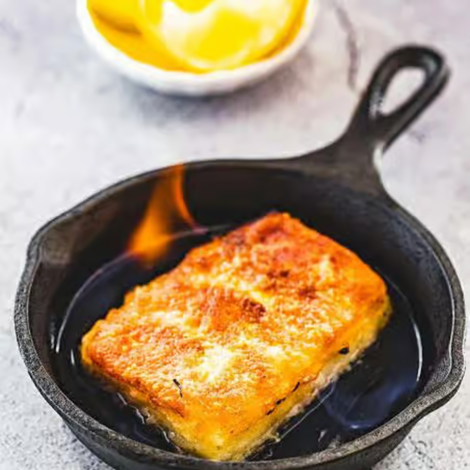 Golden, cheese-crusted baked dish served in a black cast-iron skillet, with a small bowl of yellow sauce in the background.
