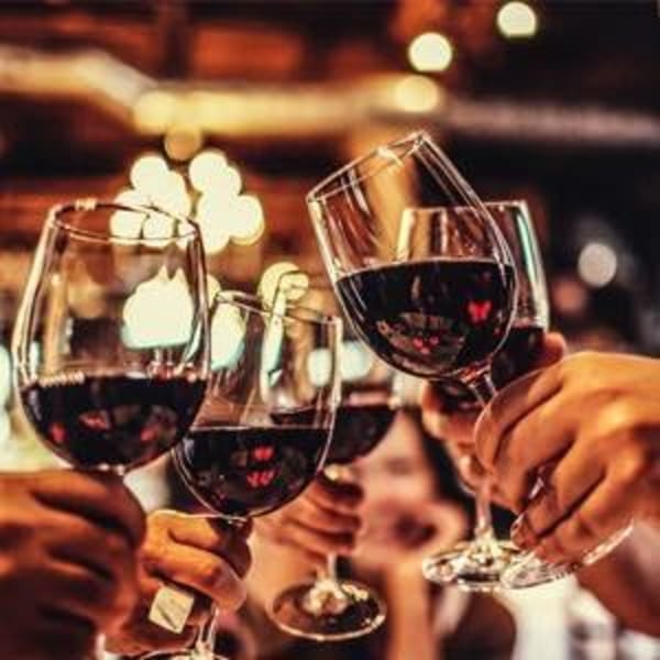 Hands holding and clinking glasses of red wine in a warm, inviting restaurant setting.