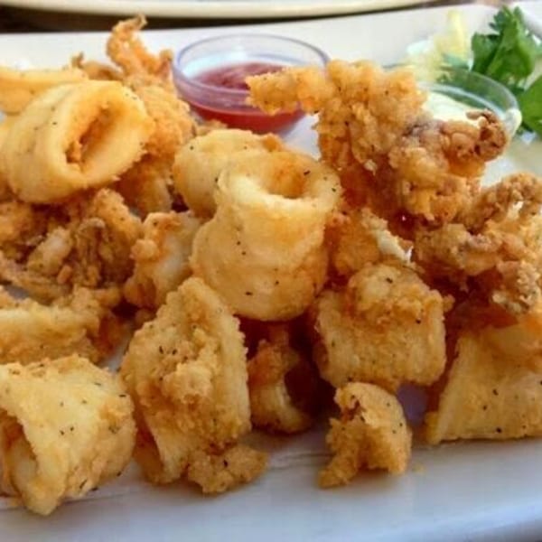 Crispy fried calamari rings and tentacles with red sauce and lemon wedges on a white plate.