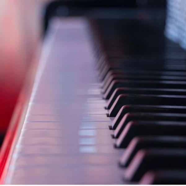 Close-up of piano keys, white and black, with a soft red and purple glow.