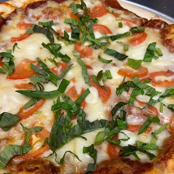 Close-up of a Vino Cappuccino Margherita pizza with melted mozzarella, sliced tomatoes, and fresh basil.
