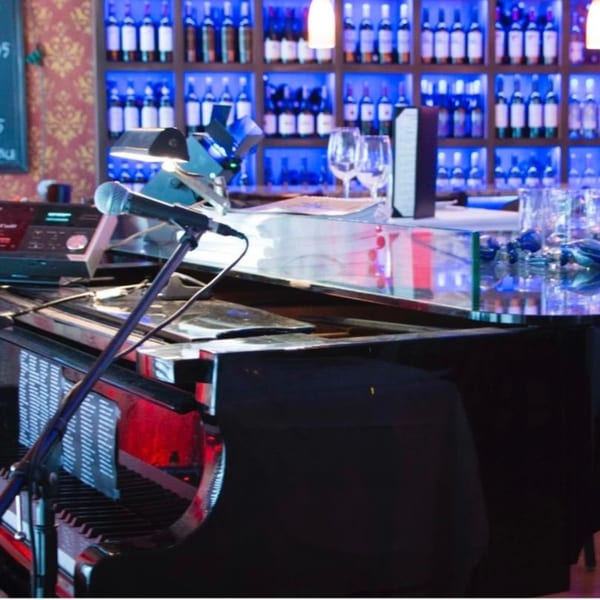 A microphone and sheet music stand on a grand piano in front of a blue-lit wine bar.