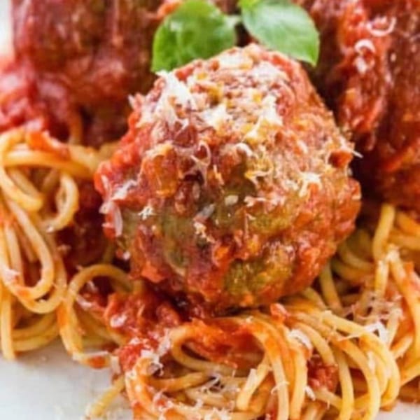 Close-up of spaghetti and meatballs, topped with red sauce, grated cheese, and a basil leaf.